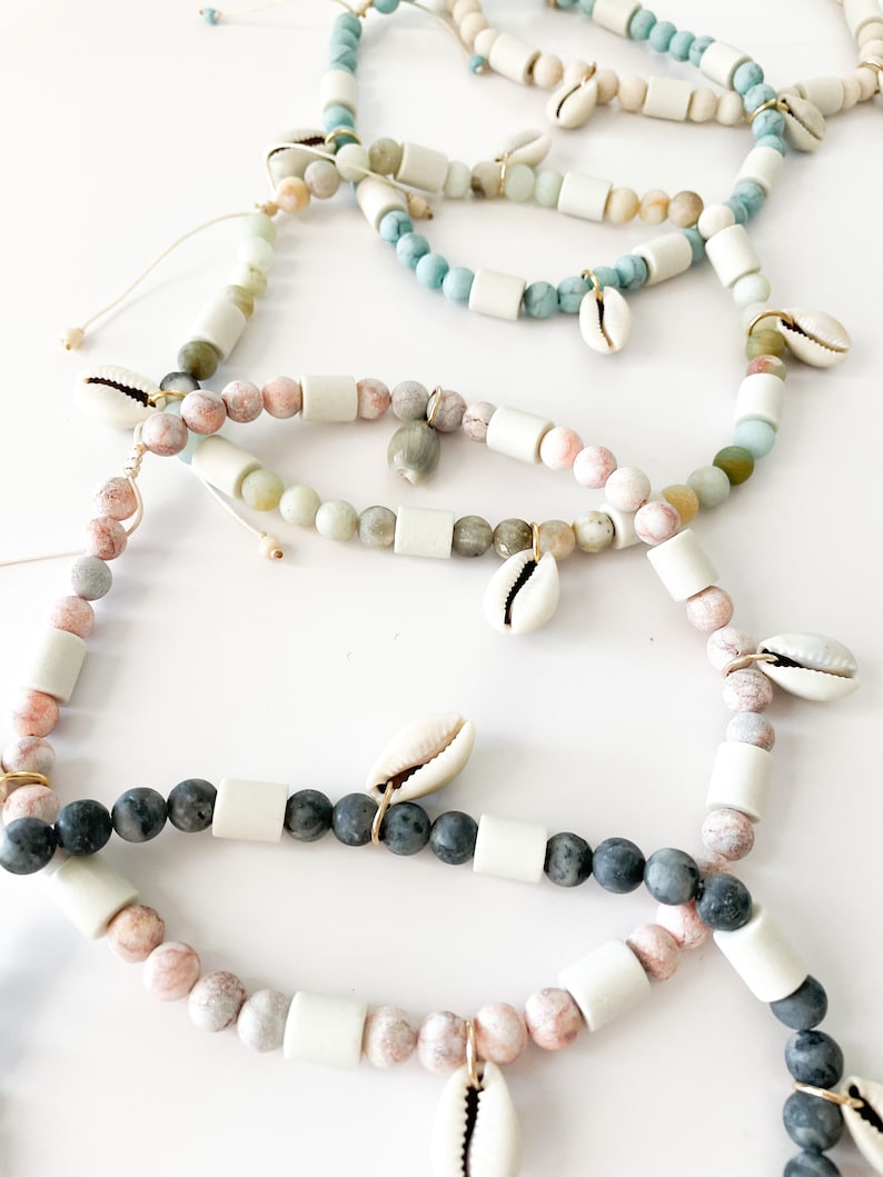 May include: A set of five bracelets featuring different colored stones and white beads. Each bracelet has a small seashell charm.