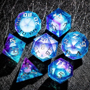 May include: Set of seven polyhedral dice in shades of blue and purple, with silver numbering. The dice are transparent, with a galaxy-like effect inside. Ideal for tabletop games, these dice are a unique and eye-catching accessory.
