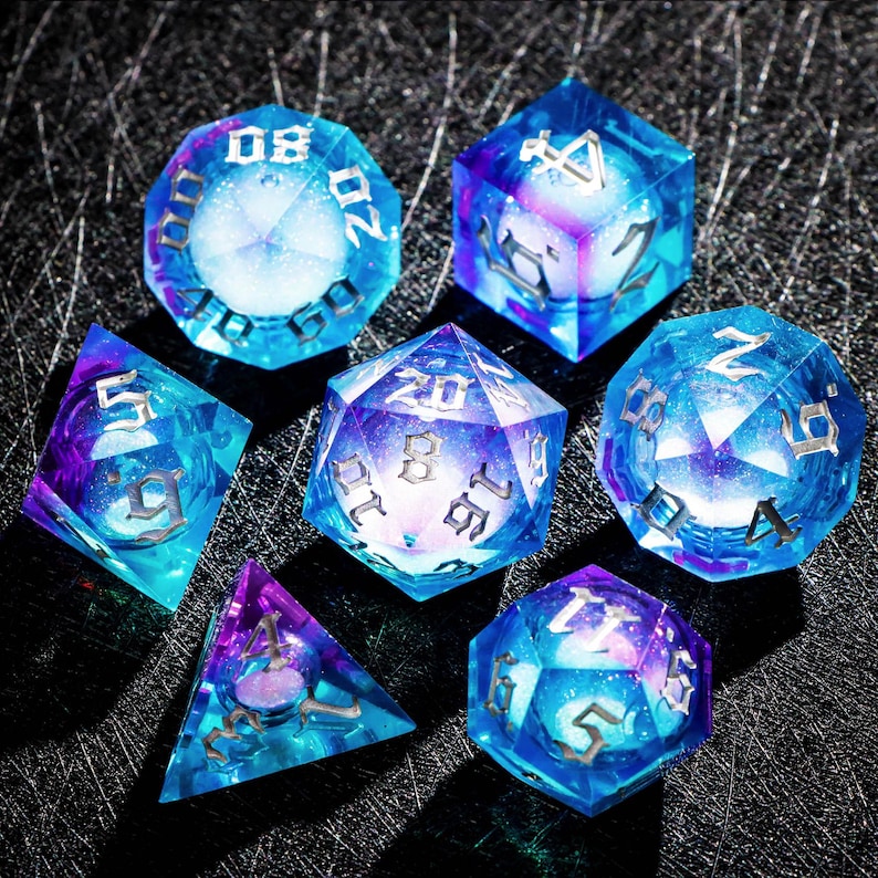 May include: Set of seven polyhedral dice in shades of blue and purple, with silver numbering. The dice are transparent, with a galaxy-like effect inside. Ideal for tabletop games, these dice are a unique and eye-catching accessory.