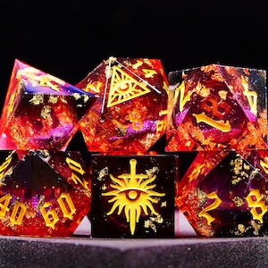 May include: Six red and gold dice with various symbols and numbers. The dice are made of clear resin with gold flakes and have a purple tint.