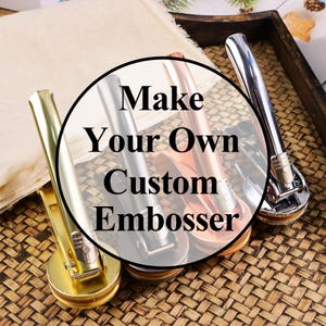 May include: An assortment of custom embossers in gold, silver, and copper tones. The embossers are arranged on a woven surface, with the text "Make Your Own Custom Embosser" in a circular design overlaying the products.