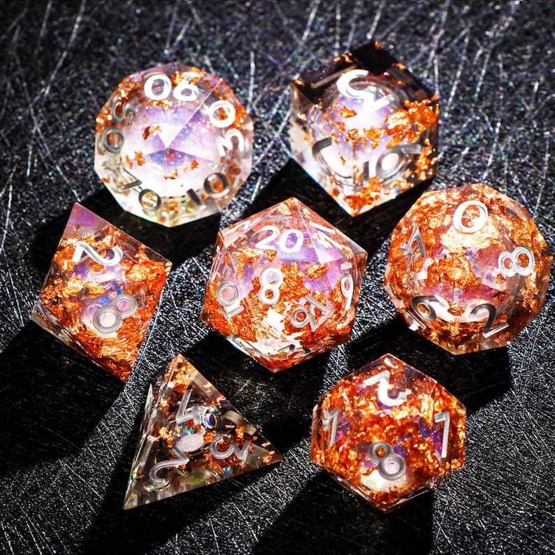 May include: Set of seven polyhedral dice with clear resin bodies, infused with copper-colored flakes. Each die features white numbering. The dice are designed for tabletop role-playing games.