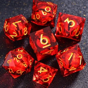May include: A set of seven translucent red polyhedral dice with gold-colored numbers. The collection includes a d20, d12, d10, d8, d6, d4, and a percentile die, all featuring sharp edges and a clear, glass-like finish with visible internal spheres.