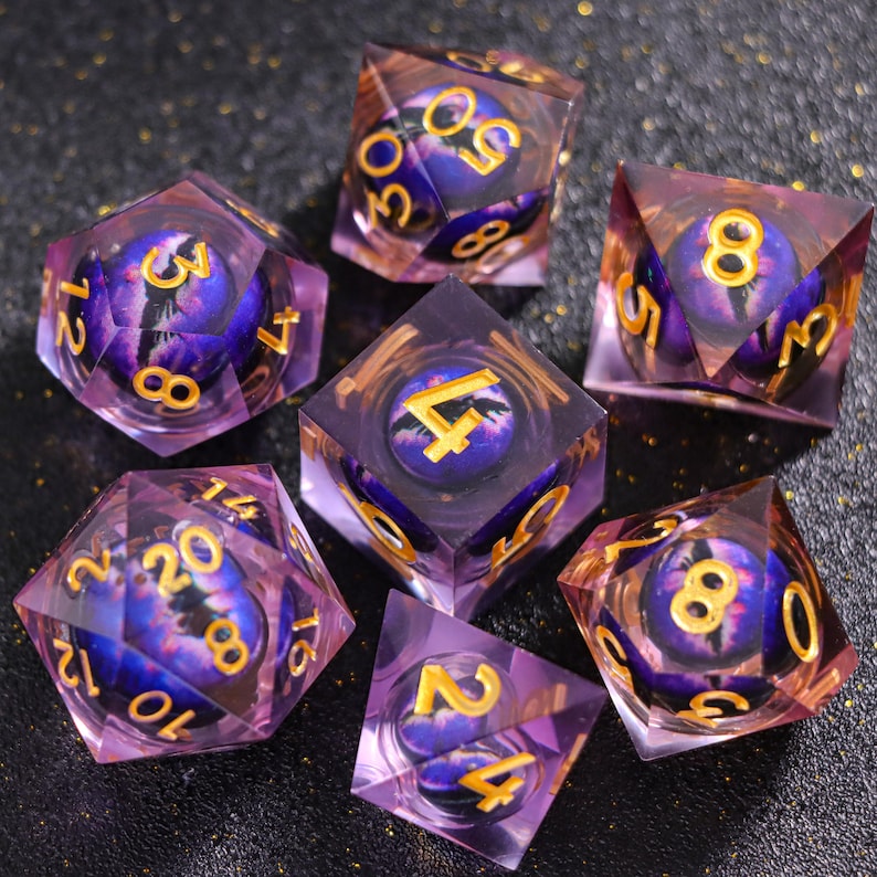 May include: A set of seven polyhedral dice made of clear purple resin, each containing a spherical insert featuring a detailed purple and blue dragon eye with a black pupil. The numbers on the dice are engraved and filled with gold-colored paint.