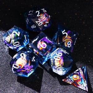 May include: A set of seven polyhedral dice with a celestial theme. The dice are transparent with a dark blue hue, and feature colorful, swirling inclusions. White numbers are visible on each face, with a vibrant, galaxy-like design.