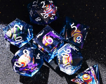May include: A set of seven polyhedral dice with a celestial theme. The dice are transparent with a dark blue hue, and feature colorful, swirling inclusions. White numbers are visible on each face, with a vibrant, galaxy-like design.