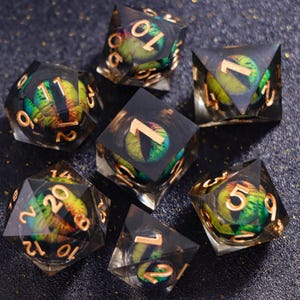 May include: A set of seven polyhedral dice made of clear resin with black edges, each containing a realistic green and yellow dragon eye with a vertical black pupil. The numbers are engraved in a metallic gold font on the outer surfaces.