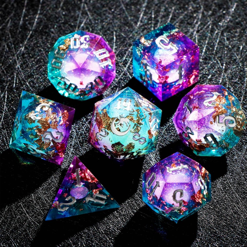 May include: Set of seven polyhedral dice in various shapes. The dice are made of clear resin with a mix of teal, purple, and gold leaf inclusions. Each die has silver numbering.