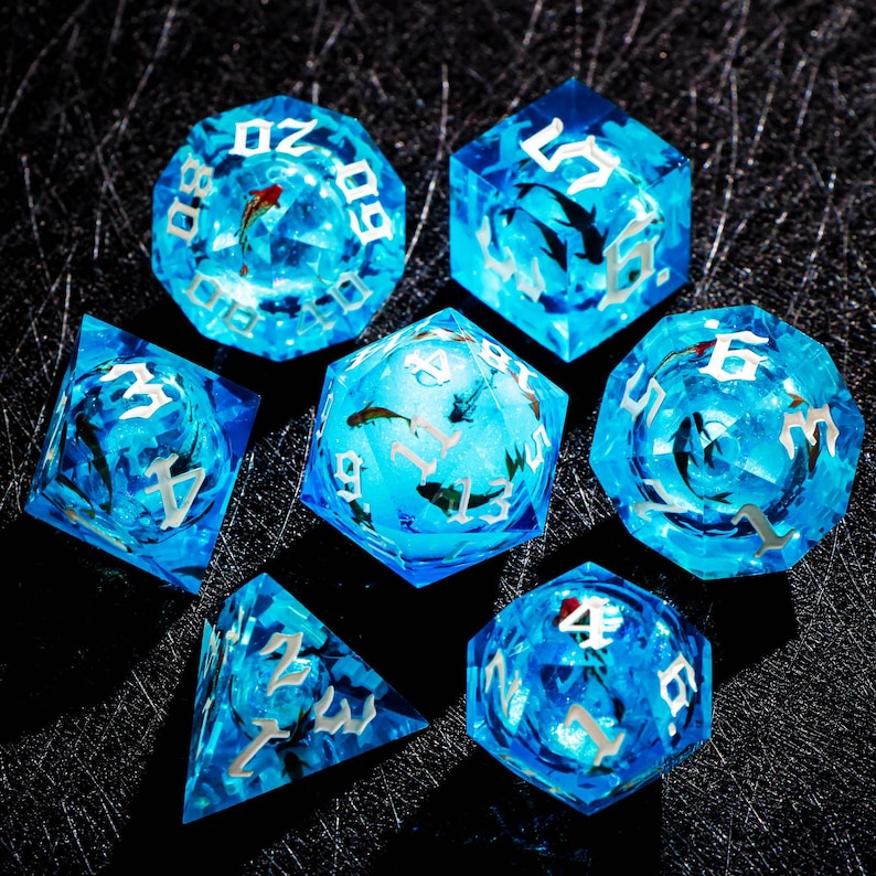 May include: Set of seven blue resin dice with embedded fish and silver numbering. The dice are various shapes, including a d20, d6, and d4, and are designed for tabletop gaming. The dice have a translucent, watery appearance.