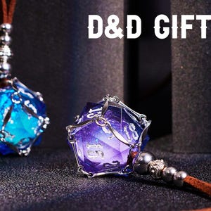 May include: Two silver caged dice pendants with iridescent blue and purple glass dice. The dice are on a brown leather cord with silver beads. The text "D&D GIFT" is in the background.