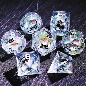 May include: A collection of clear, faceted dice with black cat illustrations and white numbers. The dice are various shapes, including a d20, d6, and d4, and have a holographic effect. The dice are designed for tabletop gaming.
