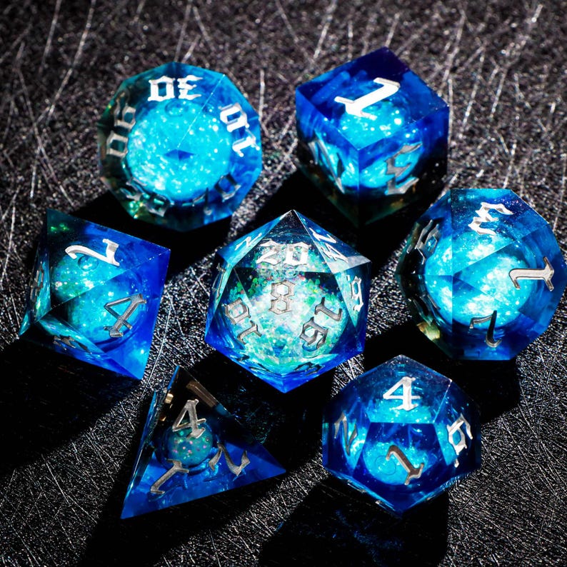 May include: A set of seven polyhedral dice with a celestial theme. The dice are a translucent blue with a swirling, galaxy-like interior. Each die has silver numbering, perfect for tabletop gaming.