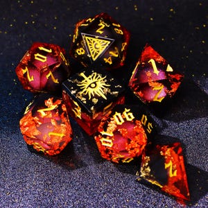 Puede incluir: Un conjunto de siete dados poliédricos de varias formas. Los dados son principalmente rojos y negros con números y detalles dorados. Algunos dados presentan símbolos de sol o triángulo. Diseñados para juegos de mesa.