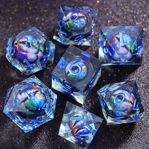 May include: A set of seven polyhedral dice made of clear resin, each containing a spherical insert with a colorful nebula-like pattern. The dice feature bright blue engraved numbers and include various geometric shapes like cubes and pyramids.