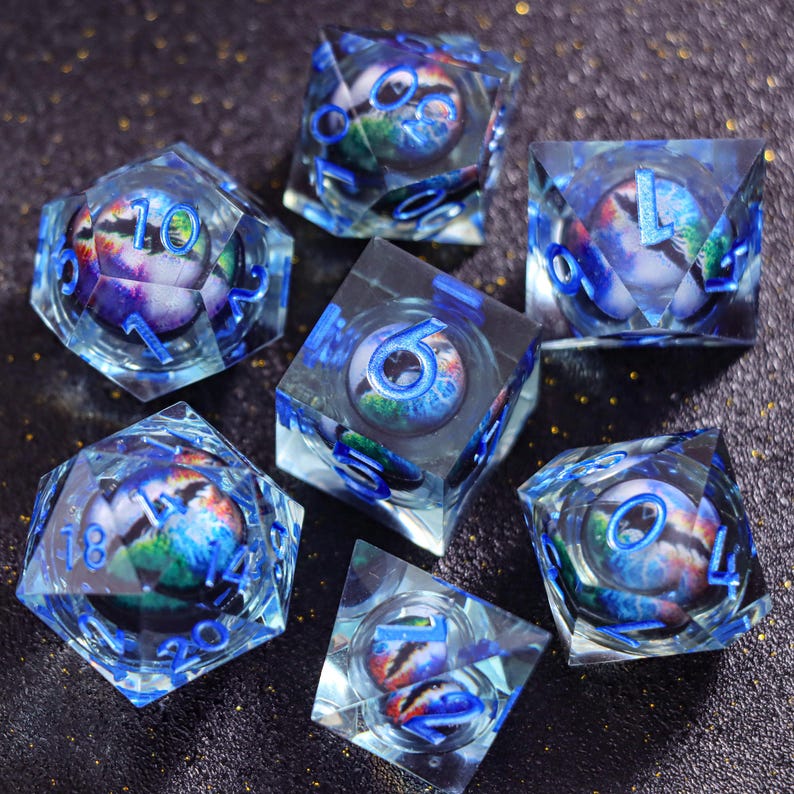 May include: A set of seven polyhedral dice made of clear resin, each containing a spherical insert with a colorful nebula-like pattern. The dice feature bright blue engraved numbers and include various geometric shapes like cubes and pyramids.