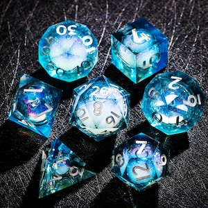 May include: Set of seven polyhedral dice in shades of blue and white, with silver numbering. The dice are transparent, with a galaxy-like design inside. The dice are for tabletop role-playing games.