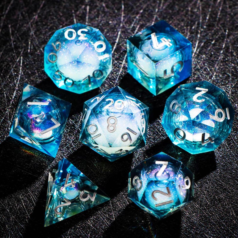 May include: Set of seven polyhedral dice in shades of blue and white, with silver numbering. The dice are transparent, with a galaxy-like design inside. The dice are for tabletop role-playing games.