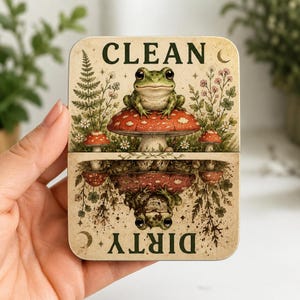 May include: A rectangular metal sign featuring a green frog sitting on a red mushroom with the word CLEAN at the top. The bottom half is an inverted mirror image of the top with the word DIRTY at the bottom, surrounded by botanical illustrations.