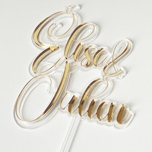 Peut inclure: Un topper de gâteau en acrylique transparent avec les noms "Lisa & Julian" écrits en lettres dorées.
