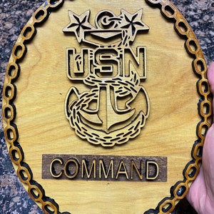 Puede incluir: Una placa de madera con un borde de cadena negra, un ancla tallada y las palabras "USN COMMAND".