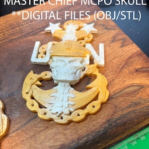 Puede incluir: Un cráneo de ancla de maestro jefe MCPO de la Marina E9 impreso en 3D en oro y blanco. El ancla está rodeada por una cadena y tiene dos estrellas en la parte superior. El texto "NAVY E9 ANCHOR" y "MASTER CHIEF MCPO SKULL" está en la parte superior de la imagen. El texto "**DIGITAL FILES (OBJ/STL)" está debajo del ancla.