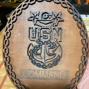 以下が含まれることがあります： 黒いチェーンの縁取り、彫刻された錨、そして「USN COMMAND」の文字が書かれた木製の銘板です。