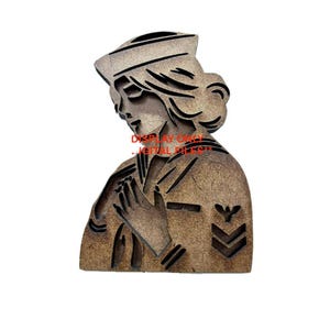 May include: A wooden cutout of a person in a sailor uniform with a hat. The person is holding their hands together in front of their chest. The cutout is brown and has a textured surface.