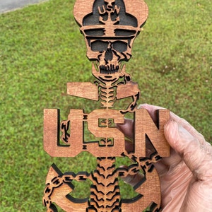 May include: A wooden cutout of a skull wearing a US Navy hat and a skeleton body with a US Navy anchor and chain. The anchor is in the shape of the US Navy logo.