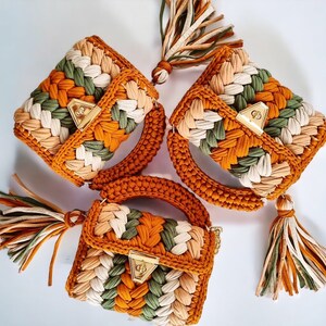 May include: Three crocheted handbags in shades of brown, green, and cream. Each bag has a unique design and features a gold metal clasp.