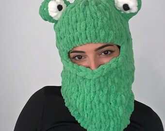 May include: Green knitted frog hat with white eyes and black pupils. The hat covers the head and face, with an opening for the eyes.