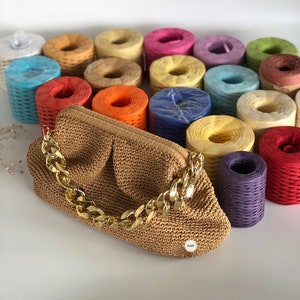 May include: A brown crocheted handbag with a gold chain strap. The bag is surrounded by colorful spools of yarn.