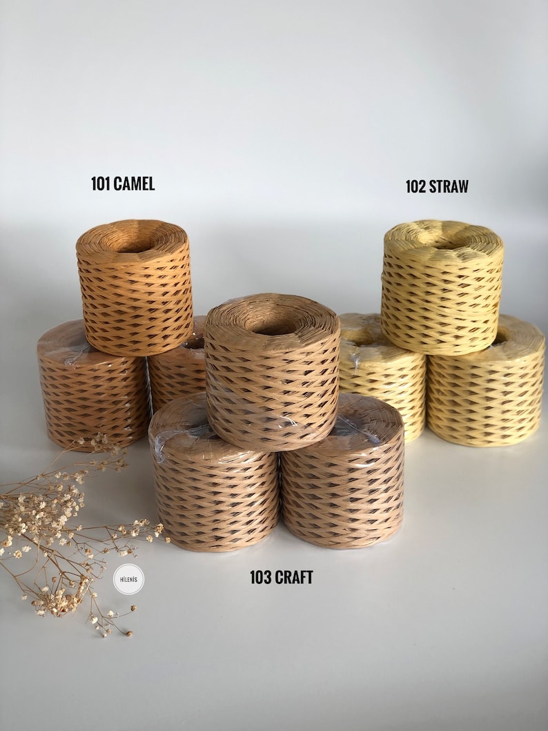 May include: Three spools of paper twine in different colors: camel, straw, and craft. The spools are stacked on a white surface.