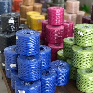 May include: A variety of colorful spools of twine, including blue, green, pink, and brown. The spools are stacked on a wooden table.