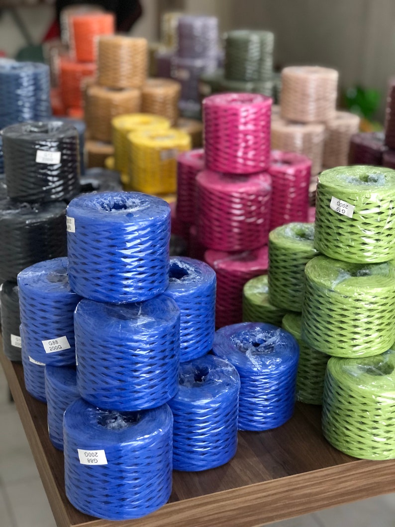 May include: A variety of colorful spools of twine, including blue, green, pink, and brown. The spools are stacked on a wooden table.