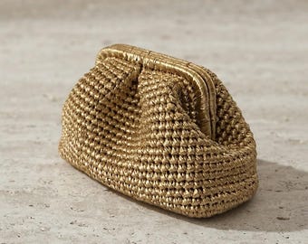 May include: A small, metallic gold clutch bag featuring a textured, crocheted exterior and a rigid, hinged frame closure. The pouch has a rounded, soft silhouette with a consistent golden sheen across the entire woven surface of the accessory.