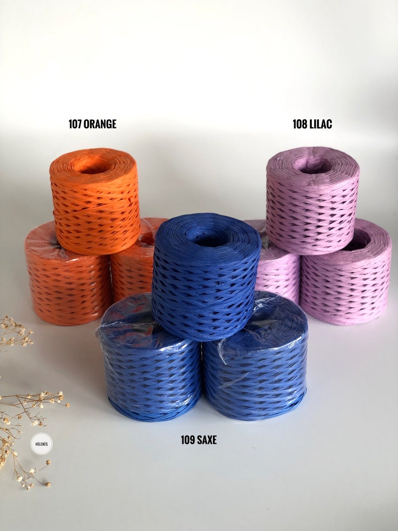 May include: Three spools of paper cord in orange, lilac, and blue. The spools are stacked on a white surface. The text "107 ORANGE", "108 LILAC", and "109 SAXE" is printed below each spool.