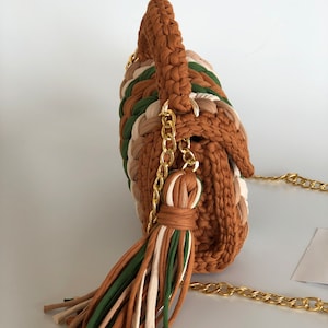May include: A brown, green, and cream crocheted handbag with a gold chain strap and tassel.