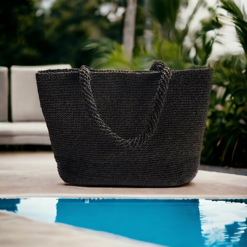 May include: A dark charcoal gray tote bag with a textured, woven appearance. The bag features a wide, open-top design and two sturdy, braided handles attached to the upper rim, providing a structured yet flexible shape for carrying various items.