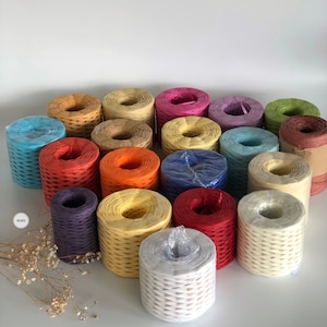 May include: Assortment of colorful paper twine spools in various colors, including blue, red, orange, yellow, green, purple, and white. The spools are arranged in a semi-circle on a white surface.