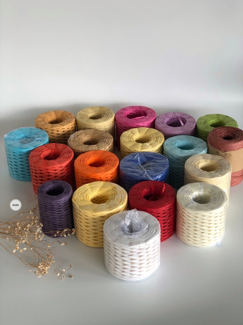 May include: Assortment of colorful paper twine spools in various colors, including blue, red, orange, yellow, green, purple, and white. The spools are arranged in a semi-circle on a white surface.