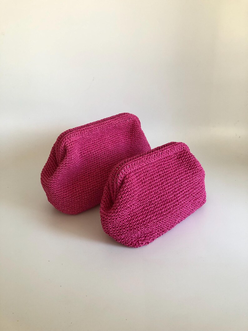 May include: Two fuchsia-colored crochet pouches with a structured frame opening. Each pouch features a dense, uniform stitch pattern and a rounded, compact shape. The bags are identical in color and texture, positioned side by side on a plain surface.