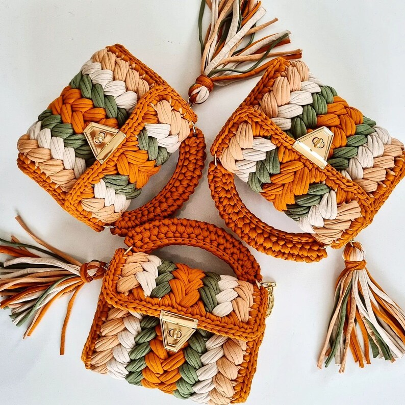 May include: Three crocheted handbags in shades of brown, green, and cream. Each bag has a unique design and features a gold metal clasp.