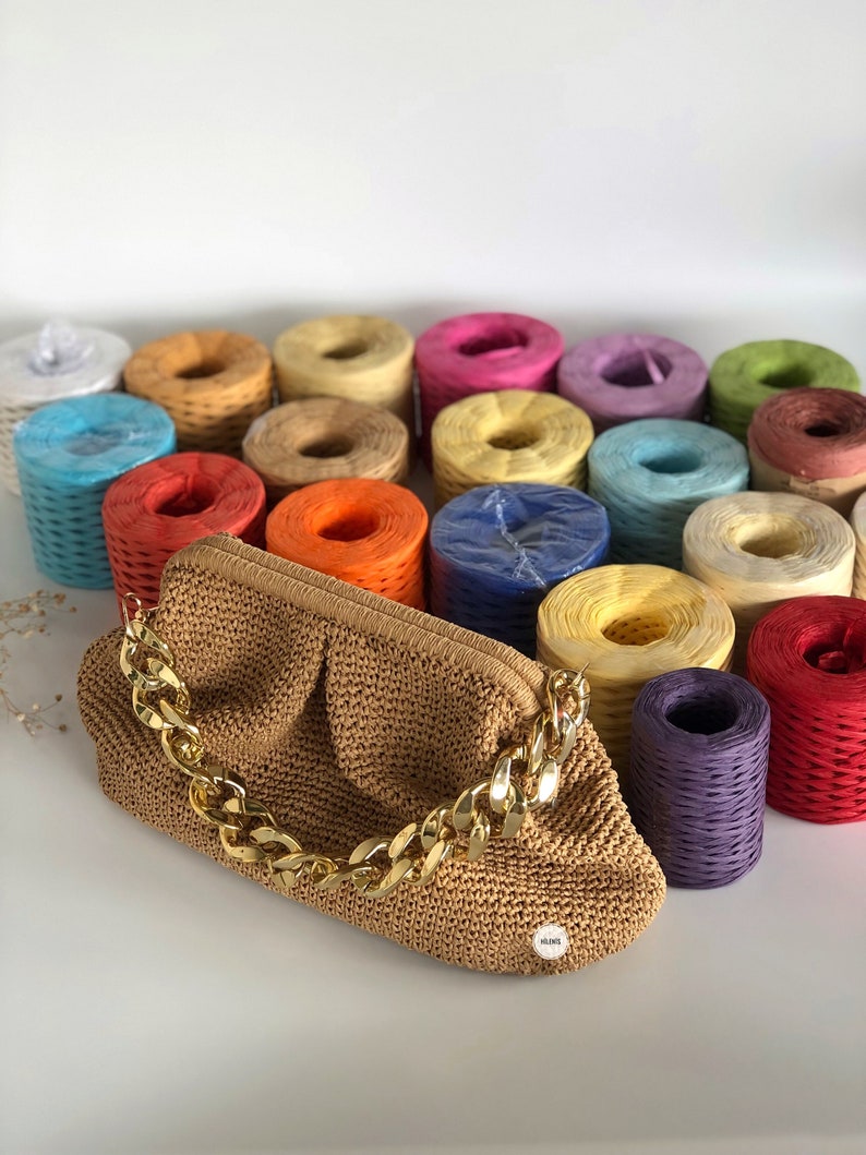 May include: A brown crocheted handbag with a gold chain strap. The bag is surrounded by colorful spools of yarn.