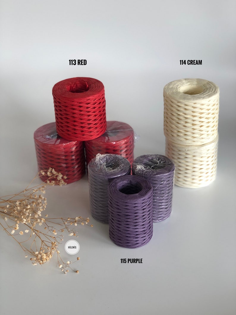 May include: Three spools of paper twine in red, cream, and purple. The spools are stacked on a white surface. The text "113 RED", "114 CREAM", and "115 PURPLE" are printed below each spool.