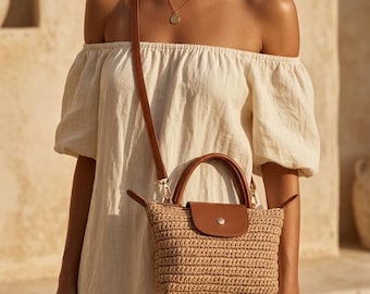 Può includere: Una borsa a mano in paglia intrecciata beige con una patta in similpelle marrone, chiusura a scatto color argento, due manici corti e una tracolla lunga regolabile marrone. La borsa presenta una base strutturata e una superficie annodata.