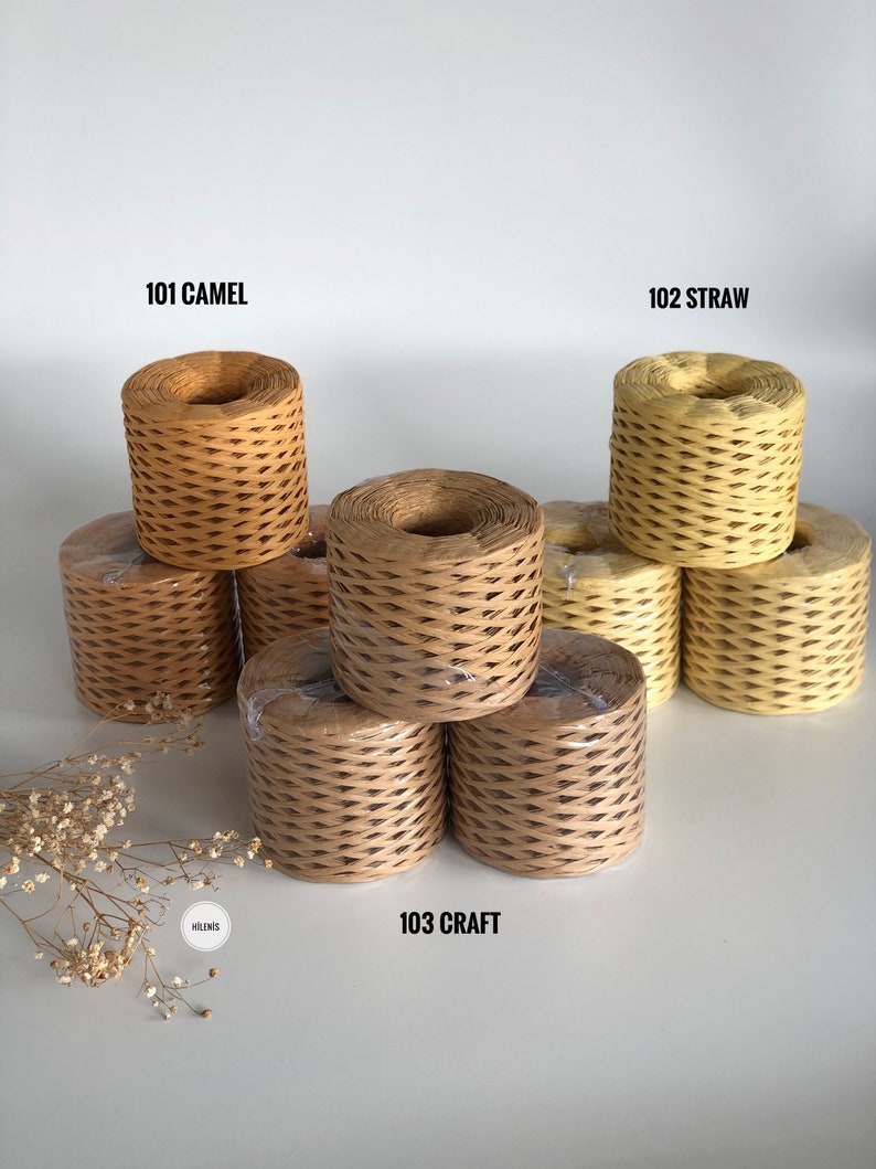 May include: Three spools of paper twine in different colors: camel, straw, and craft. The spools are stacked on a white surface.