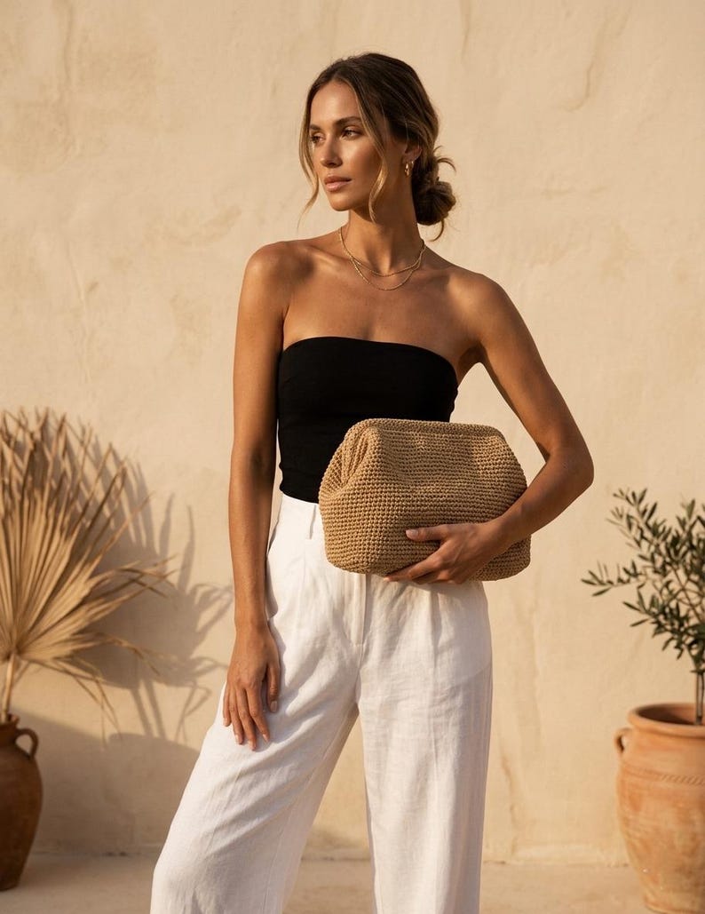 Puede incluir: Un bolso de mano tejido en color beige con una abertura de marco estructurado. El bolso presenta un exterior texturizado de ganchillo en un tono tostado neutro, una forma rectangular con esquinas redondeadas y un cierre superior articulado.