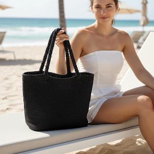 May include: A solid black tote bag with a textured, woven surface and two sturdy, braided handles. The bag features a structured, rectangular base and an open top design, providing a spacious interior compartment for carrying various personal items.