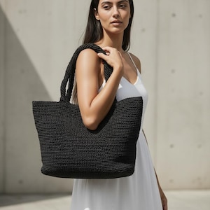 May include: A black tote bag with a textured, woven construction and two sturdy shoulder straps. The bag features a rectangular shape with a wide opening and a consistent, dense knit pattern throughout the exterior surface of the accessory.
