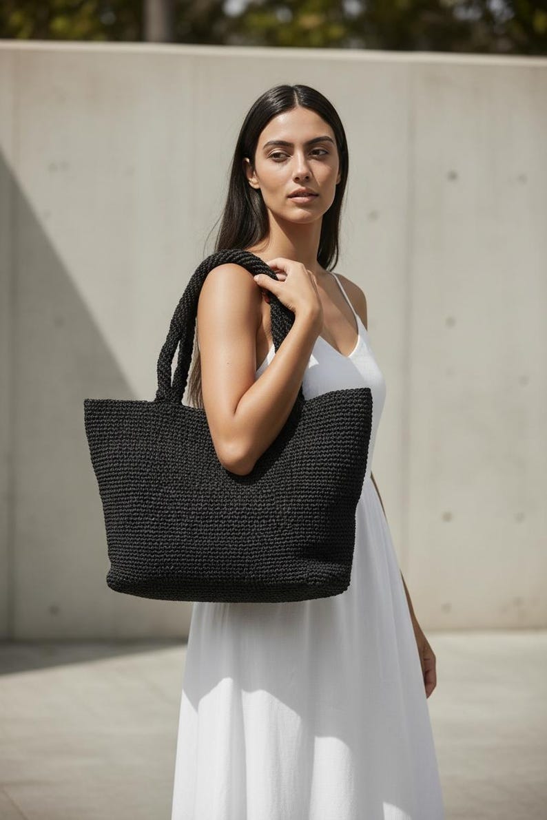 May include: A black tote bag with a textured, woven construction and two sturdy shoulder straps. The bag features a rectangular shape with a wide opening and a consistent, dense knit pattern throughout the exterior surface of the accessory.